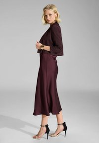 Top corto burdeos con un sutil brillo, combinado con una falda de satén burdeos fluida. Tacones de aguja con strap negro y acento beige.