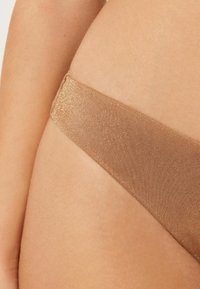 Nude-farbene Bikinihose aus glattem, glänzendem Stoff. Sie verfügt über einen dünnen, strukturierten Bund, der in einen dreieckigen Schnitt übergeht.