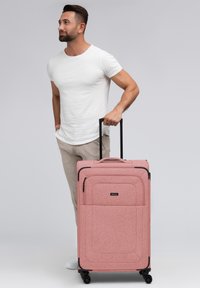 Roze stoffen koffer met een gestructureerd oppervlak, zwarte accenten, bovenhandvat, uitschuifbaar handvat en vier wielen voor wendbaarheid.