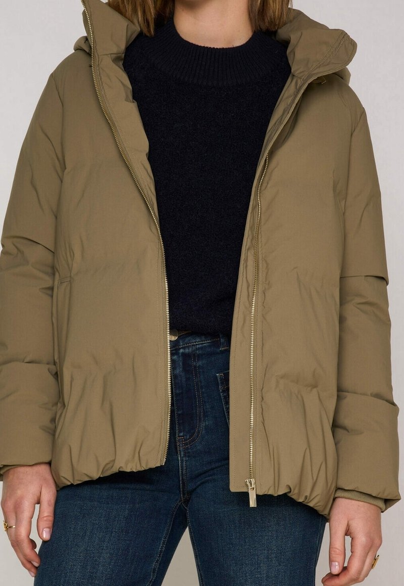 Olivově zelená péřová bunda s kapucí, lehký materiál, přední zip a boční kapsy, kombinována s tmavým svetrem a džíny.