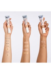 Kolme eri ihonsävyistä kättä pitää CC+ Nude Glow -meikkivoideputkia, joista jokaisessa näkyy useita meikkivoidesävyjä käsivarressa testattuna.