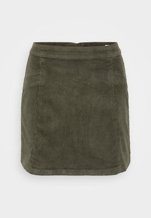 Tumes roheline valgest kummist mini seelik, millel on struktureeritud disain, tasane vöökoht ja peened õmblused detailideks.