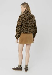 Veste courte en imprimé léopard marron et noir, avec un col montant et des poignets élastiques, associée à une jupe en velours côtelé beige et des chaussettes à motifs.