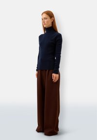 Pullover a collo alto blu navy abbinato a pantaloni marroni a gamba larga. Il pullover presenta maniche lunghe e una vestibilità slim. Texture a maglia liscia visibile.