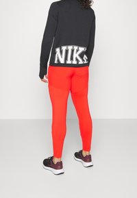 Zwarte sporttop met groot wit "NIKE" logo op de achterkant, gecombineerd met felrode leggings en zwart-paarse hardloopschoenen.