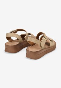 Sandalias de plataforma beige con tiras entrecruzadas, un acento de hebilla y una suela texturizada. El material superior suave complementa el diseño elevado.