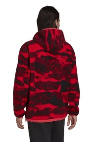 Röd och svart mönstrad fleecehoodie med dragsko i huvan, texturerat material och elastisk midja. Har en avslappnad passform och långa ärmar.