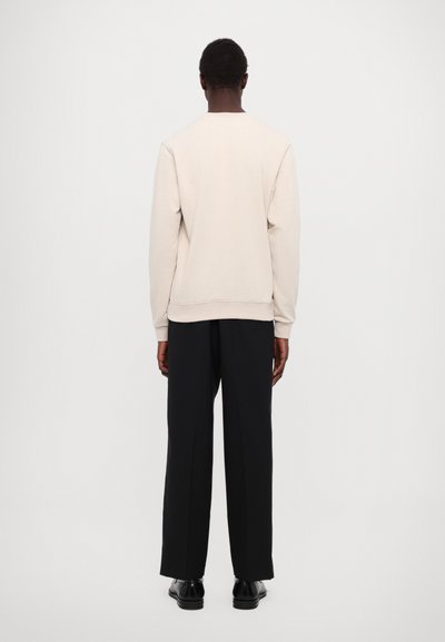 Beige sweatshirt med rund hals, ribbede mansjetter og liv. Kombinert med løstsittende svarte bukser og svarte sko.