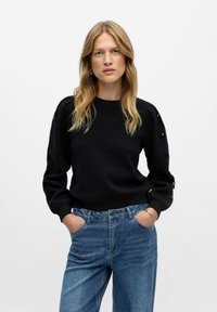 Maglione nero con maniche a sbuffo testurizzate e dettagli a taglio. Abbinato a jeans in denim blu chiaro a vita alta per un fit rilassato.