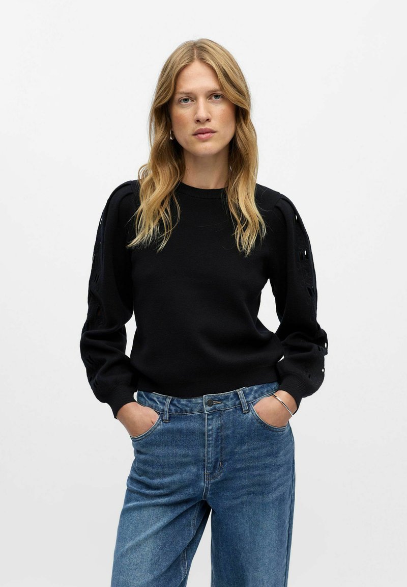 Maglione nero con maniche a sbuffo testurizzate e dettagli a taglio. Abbinato a jeans in denim blu chiaro a vita alta per un fit rilassato.