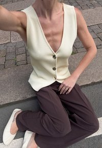 Cream ribbed vest with a deep V-neck and four large buttons; paired with loose brown trousers and white ballet flats.