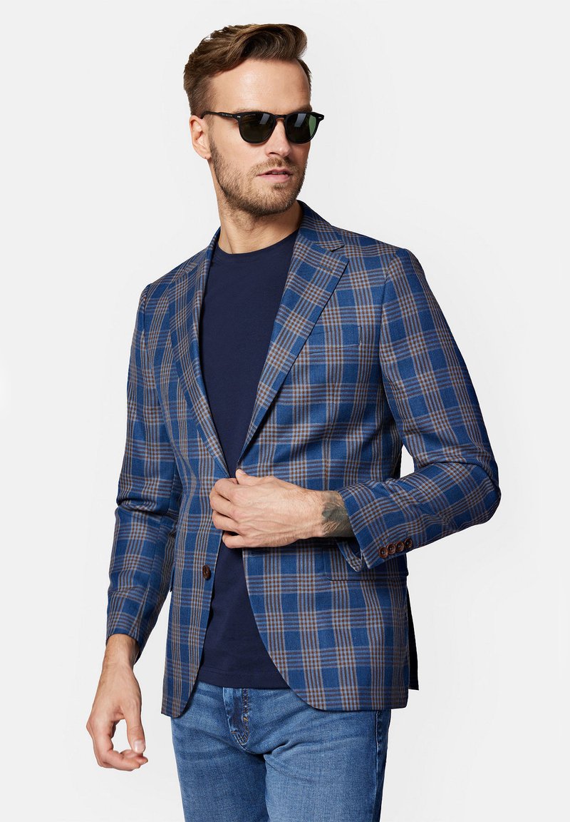 Niebieska marynarka w kratę z brązowymi akcentami, dopasowany krój, klapy notch, zapięcie na jeden guzik, noszona na granatowej koszuli, w zestawie z dżinsami.
