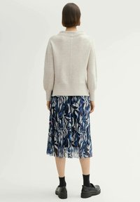 Maglione grigio chiaro a costine con collo alto, abbinato a una gonna blu trasparente con motivo a fiori astratti e scarpe con plateau nere.