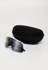 Gafas de sol con montura transparente y lentes oscuros degradados, descansando junto a un estuche rígido negro con cremallera. Textura suave, diseño moderno.