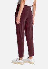 Bordeaux tapered byxor med en mjuk textur, elastisk midja och sidofickor, kombinerat med vita sneakers.