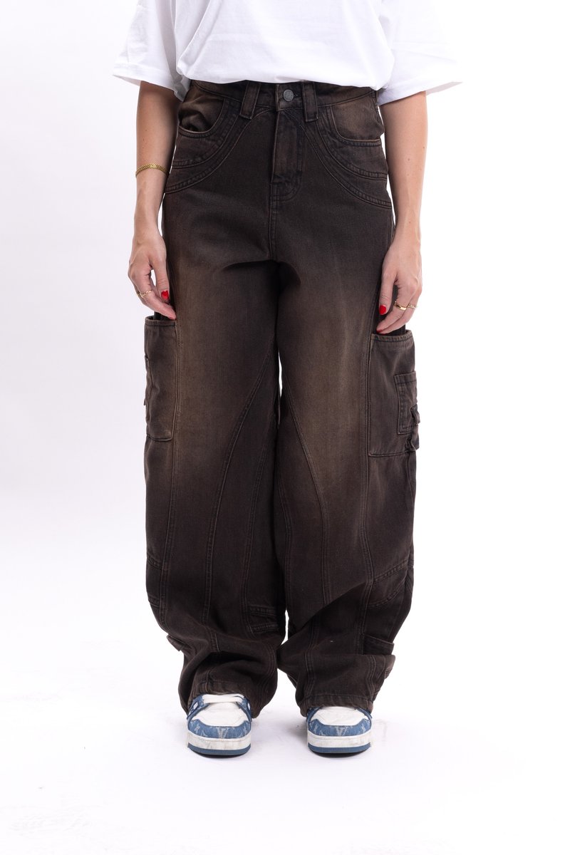 Spodnie cargo w ciemnym brązowym dżinsie o luźnym kroju, z wysokim stanem, wieloma bocznymi kieszeniami i przeszyciami, zestawione z niebieskimi i białymi sneakersami.