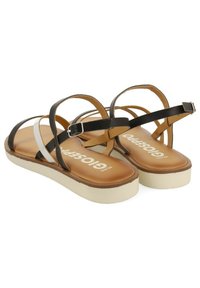 Sandalias de tiras en blanco y negro con una plantilla marrón y suela clara, que cuentan con un detalle de hebilla y una textura suave.