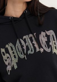 Felpa nera con capuccino con la parola "SPOILED" in grandi strass. Include un cappuccio con cordino e tessuto testurizzato.