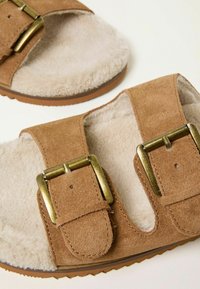 Braune Wildledersandalen mit doppelt verstellbaren Schnallen und einem weichen, cremefarbenen Fleece-Futter. Strukturiertes Sohlenprofil für guten Halt und Komfort.