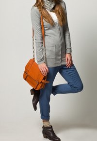 Grå cardigan med knappar, vit topp, blå byxor, orange läderväska, mörkbruna ankellånga stövlar och en mönstrad scarf runt nacken.