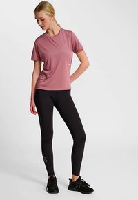 Hellrosa sportliches T-Shirt mit kurzen Ärmeln und Rundhalsausschnitt, kombiniert mit schwarzen Leggings. Die Leggings haben ein dezentes Logo seitlich.