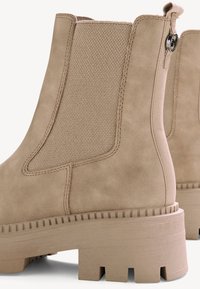 Beige ankle boots with a textured finish, elastic side panels, and a chunky heel featuring vertical grooves for traction.