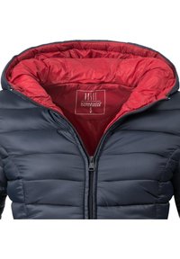Doudoune marine avec une doublure intérieure rouge, au design matelassé, col haut et fermeture éclair à l'avant. Fabriquée en matériau lisse et résistant à l'eau.