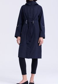 Manteau à capuche bleu marine avec une taille ceinturée, doté de poches latérales et d'une coupe droite. Confectionné dans un tissu léger et texturé.