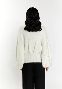 Kremowy, oversize'owy sweter o teksturowanym splocie, z bufiastymi rękawami ozdobionymi równomiernie rozmieszczonymi koralikami oraz prążkowanym dołem.