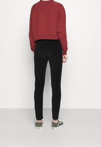 Röd kort sweatshirt med rund halsringning, i kombination med svarta tajta jeans. Grå sneakers med vit sula och logotypdetalj.