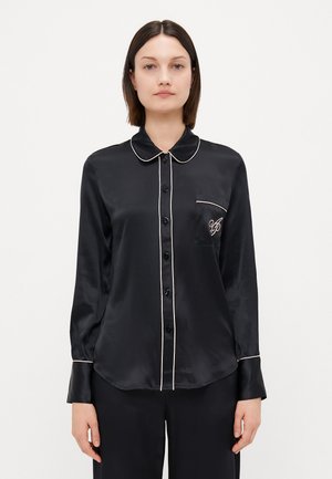 Sort satin skjorte med klassisk krave, lange ærmer, knaplukning foran og hvide pipede detaljer. Har en enkelt brystlomme og broderet detalje.
