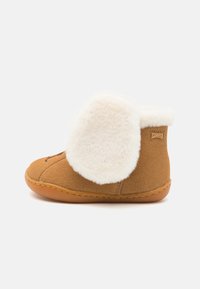 Brune semsket ankelstøvler med en fluffy hvit pelskant, gummisåle og sammenføyningsdetaljer, med et merke på siden.