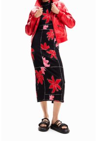 Veste en cuir rouge superposée sur une robe midi noire avec une broderie florale vive en rouge et rose. Sandales noires avec des accents tressés.