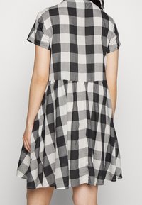 Robe à carreaux noir et blanc avec des manches courtes et une taille froncée, en tissu léger, présentant un design de jupe évasée.