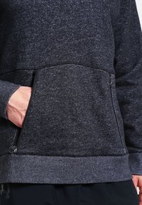 Felpa grigio scuro con un tessuto testurizzato, dotata di una tasca con zip sul davanti e polsini e orlo a costine. Finitura liscia nel complesso.
