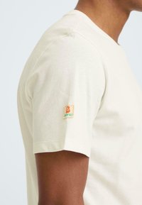 T-shirt in crèmewit gemaakt van katoen, met een ronde hals en korte mouwen. Opvallend klein logoplaatje op de linker mouw.