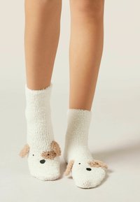 Chaussettes blanches et pelucheuses avec un design de visage de chien, présentant des accents beiges pour les oreilles et un nez noir, texture rembourrée et hauteur mi-mollet.