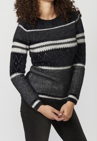 Stickad tröja i svart och grått med horisontella ränder och ett diamantmönster, med rund halsringning och åtsittande muddar.