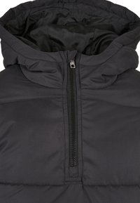 Doudoune noire avec un col montant et une fermeture éclair frontale mi-longue, montrant une texture de tissu matelassé et rembourré.