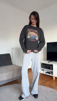 Μαύρο φούτερ με γραφικό "Ripcurl Hawaii", σετ με ανοιχτό γκρι φόρμα, φορεμένα από άτομο σε περιβάλλον σαλονιού.