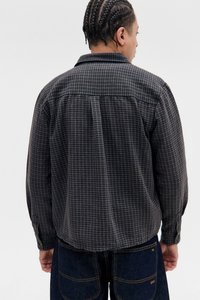 Sort og grå rutete skjorte med lange ermer, kneppede mansjetter og avrundet kant, laget av et teksturert stoff. Ser slitt ut fra baksiden.