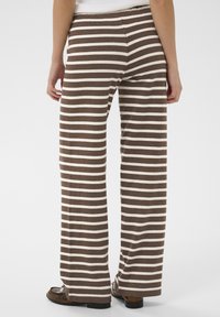 Hnedé a krémové pásikavé široké nohavice, vyrobené z mäkkej látky, s hladkou textúrou a uvoľneným strihom, s pásom a minimálnym zdobením.