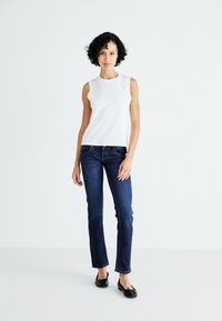 Hvit ermeless topp med dekorasjoner på skuldrene, kombinert med mørkeblå rette jeans og svarte ballerinasko.