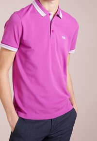 Polo shirt rose avec des accents blancs et une patte de boutonnage à deux boutons. Manches courtes avec un bord contrastant, fabriqué en tissu de coton lisse.