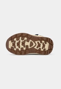 Semelle en caoutchouc marron et beige d'une chaussure robuste avec des semelles profondes, idéale pour une utilisation en extérieur ou en randonnée.