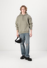 Green hooded sweatshirt, front pocket, light blue distressed jeans, black chunky shoes, and a small black bag with a strap.