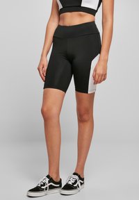 Mustavalkoiset urheilu shortsit, joissa on korkea vyöt ärö, tyylikäs muotoilu ja sileä pinta, yhdistetty mustiin lenkkareihin.