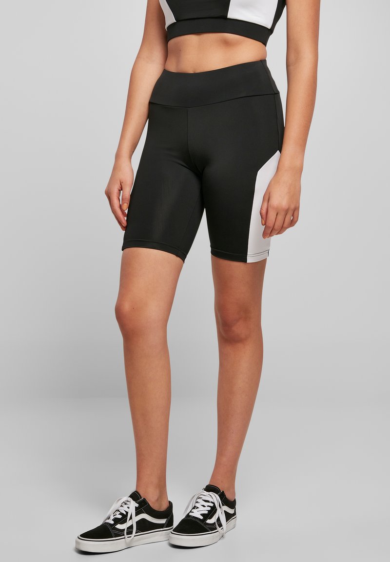 Mustavalkoiset urheilu shortsit, joissa on korkea vyötärö, tyylikäs muotoilu ja sileä pinta, yhdistetty mustiin lenkkareihin.