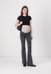 Top negro de manga corta, banda de jersey gris en la barriga, jeans acampanados grises y botines negros. La modelo sostiene un bolso negro. Fondo neutro.