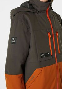 Herren Outdoor-Jacke in Dunkelgrau und Orange, mit Kapuze, durchgehendem Reißverschluss, zwei Brusttaschen und Logo-Akzenten. Das Material scheint wasserdicht zu sein.